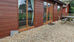 Un bâtiment en bois doté de grandes portes coulissantes en verre, d’une terrasse en bois et d’une table de pique-nique.