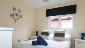 Un lit bien fait, avec une literie blanche et deux oreillers, une table de chevet avec une lampe et un élément décoratif mural.