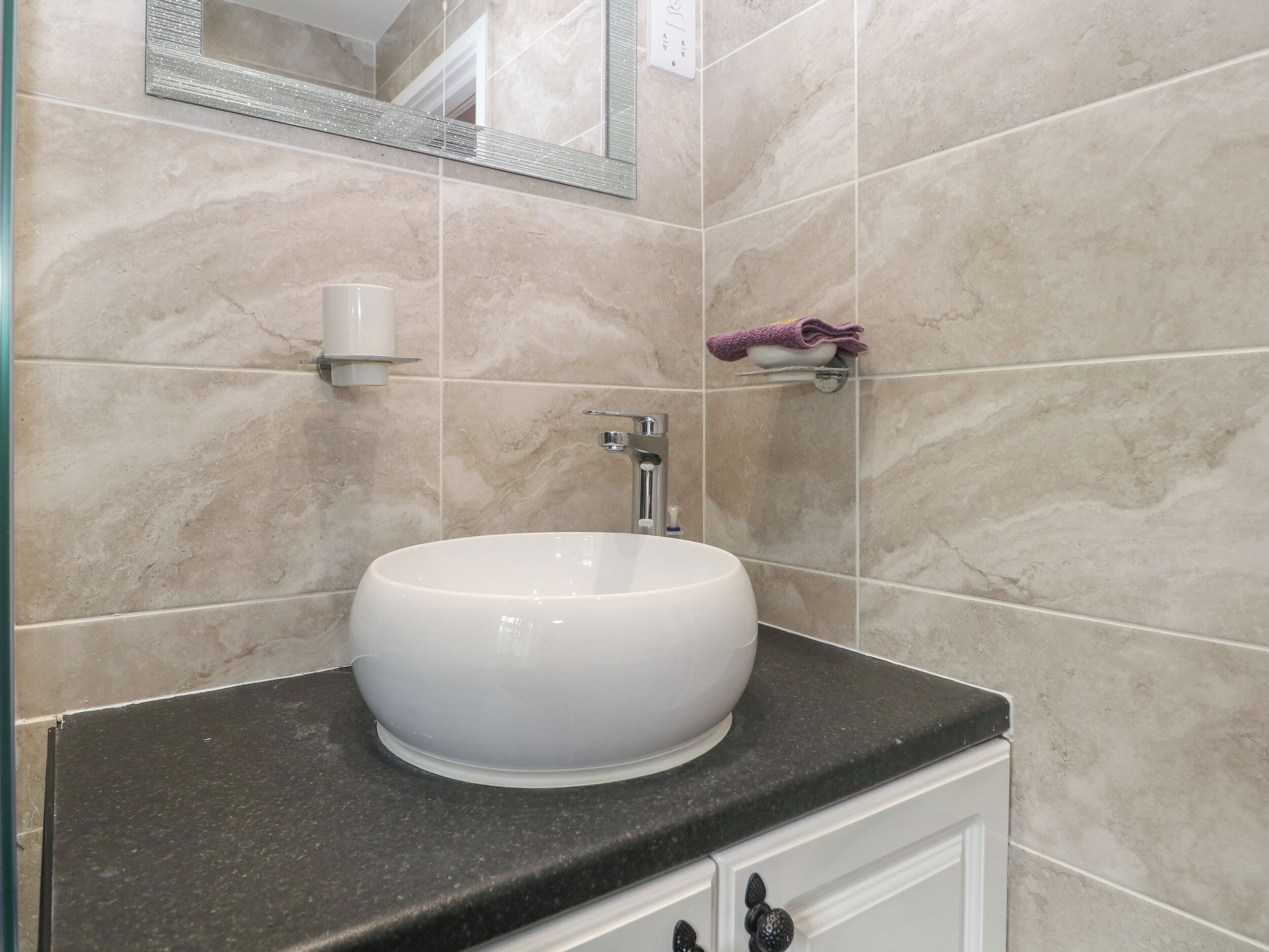 A bathroom with a white sink, black countertop, and beige tiles.