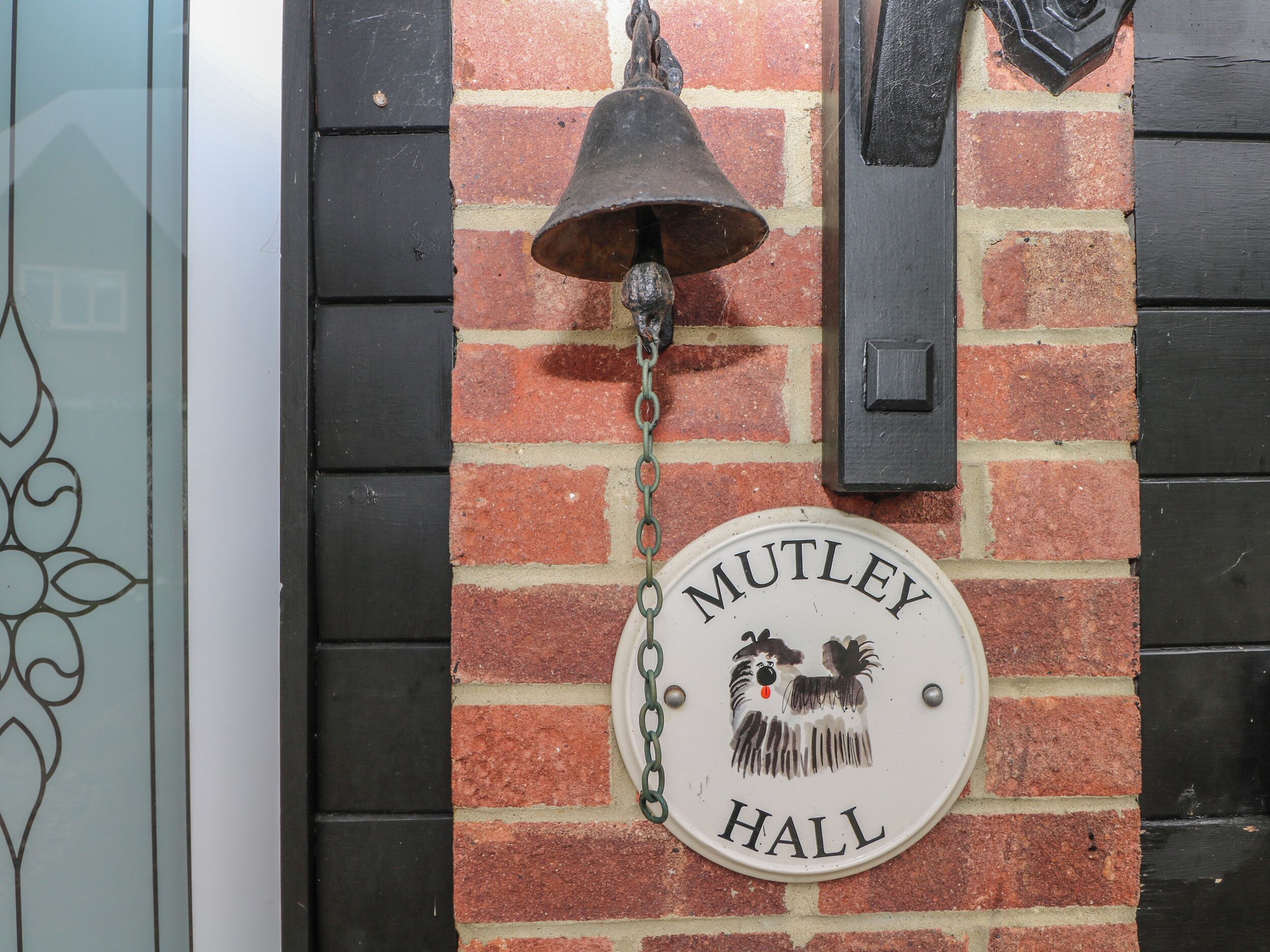 A brick wall with a sign reading "Mutley Hall" and a hanging bell.