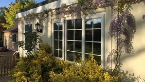Une maison à l’extérieur blanc, dotée de grandes fenêtres et de plantes grimpantes aux fleurs violettes.