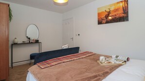Ein Schlafzimmer mit Bett, Nachttisch, Stuhl, Schreibtisch, Spiegel und einem Bild an der Wand.