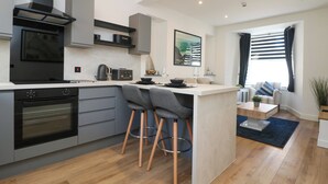 A modern kitchen with a central island, built-in oven, and a black range hood. - Savoy Bay (Helston)