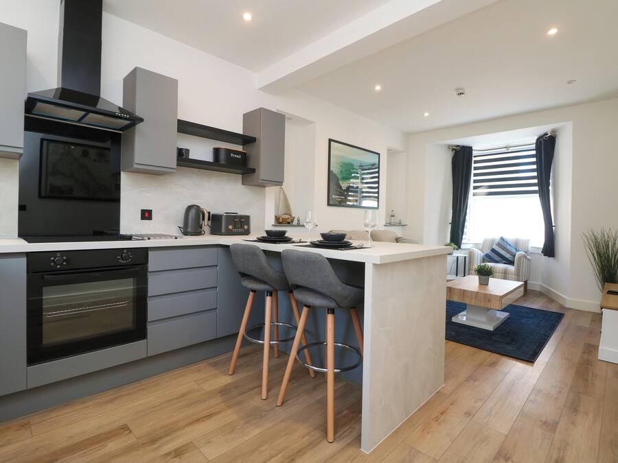 A modern kitchen with a central island, built-in oven, and a black range hood.