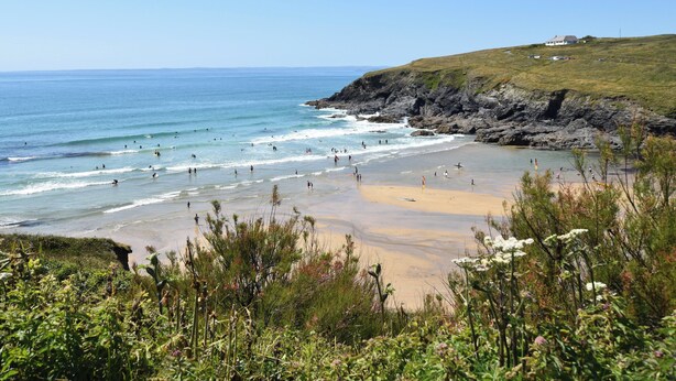 A coastal beach with rocky cliffs, a sandy shore, and lush greenery. - Savoy Bay (Helston)