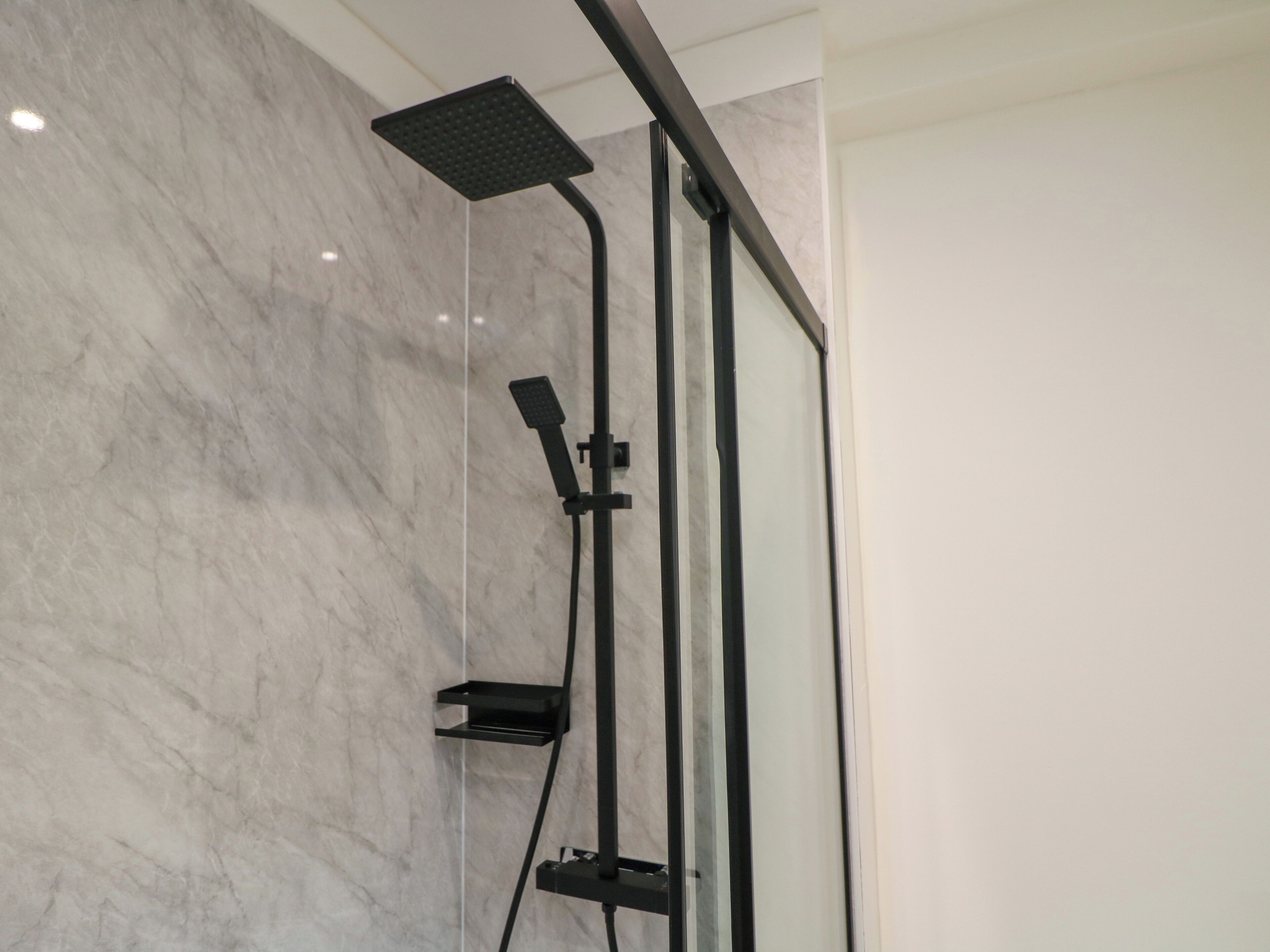 Un baño moderno con cabina de ducha de vidrio, un cabezal de ducha de mano y panel de control en la pared.