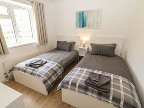 A room with two single beds, a small bedside table with a lamp, a window with curtains, and a painting on the wall.