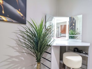 Um banheiro moderno com toucador branco, um espelho grande, uma planta em vaso e um banco branco.