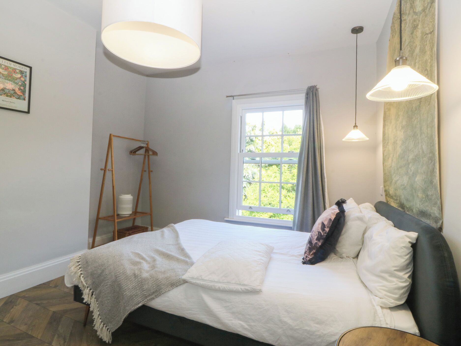 A bedroom with a bed, a window with curtains, a hanging light fixture, and a wooden ladder against the wall.