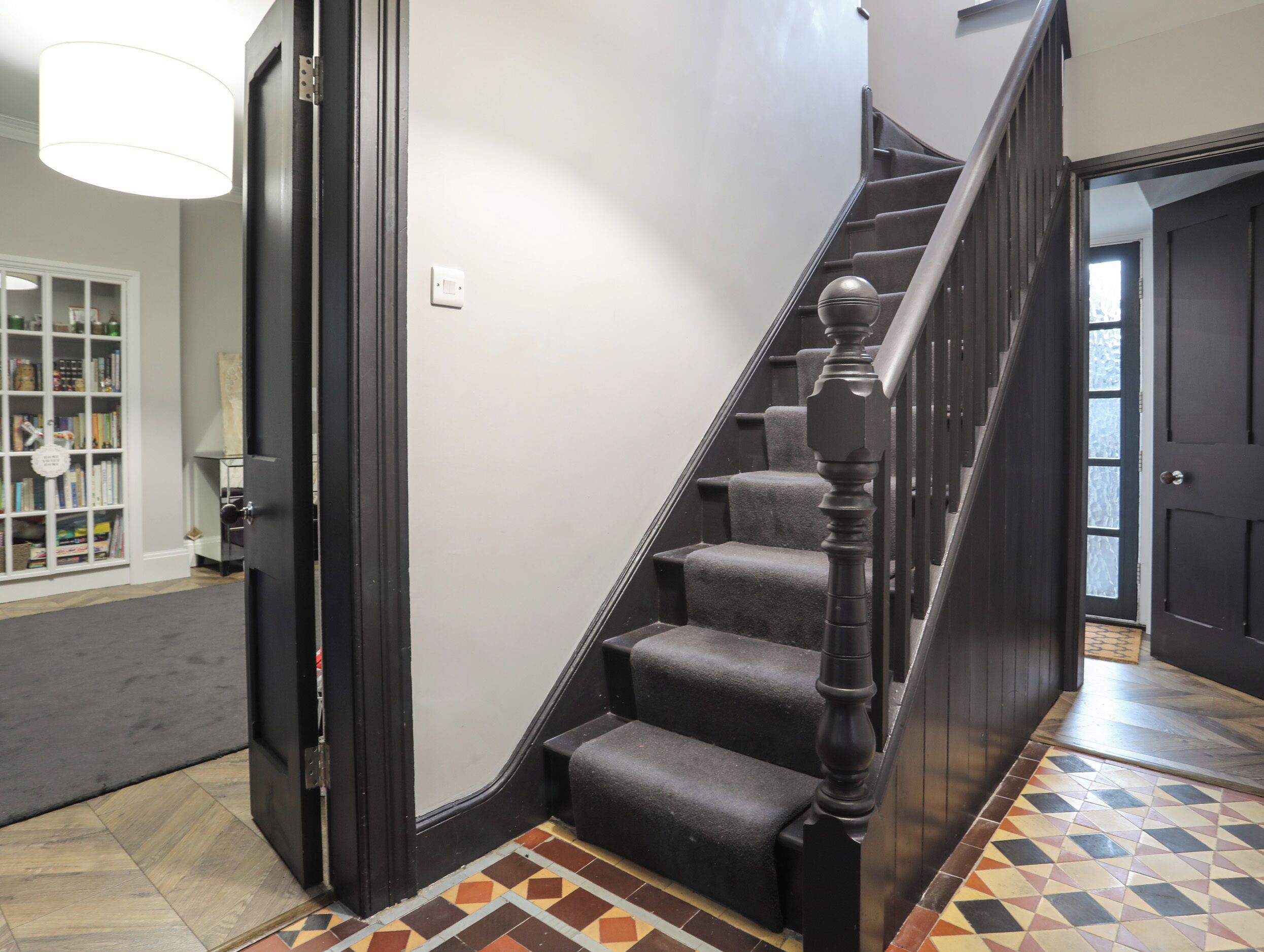 Un escalier avec une rampe noire et des marches recouvertes de moquette, menant à un palier.