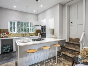 A modern kitchen with a central island, bar stools, and a view of the outdoors. - Gweryl Lodge (Conwy)