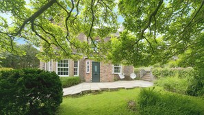 Une maison en briques avec une porte verte, un petit jardin devant et un escalier menant à l’entrée.