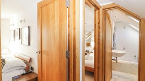 A hotel room with a wooden door, a bed with a headboard, a bedside table with a remote control, and a wall-mounted light fixture.