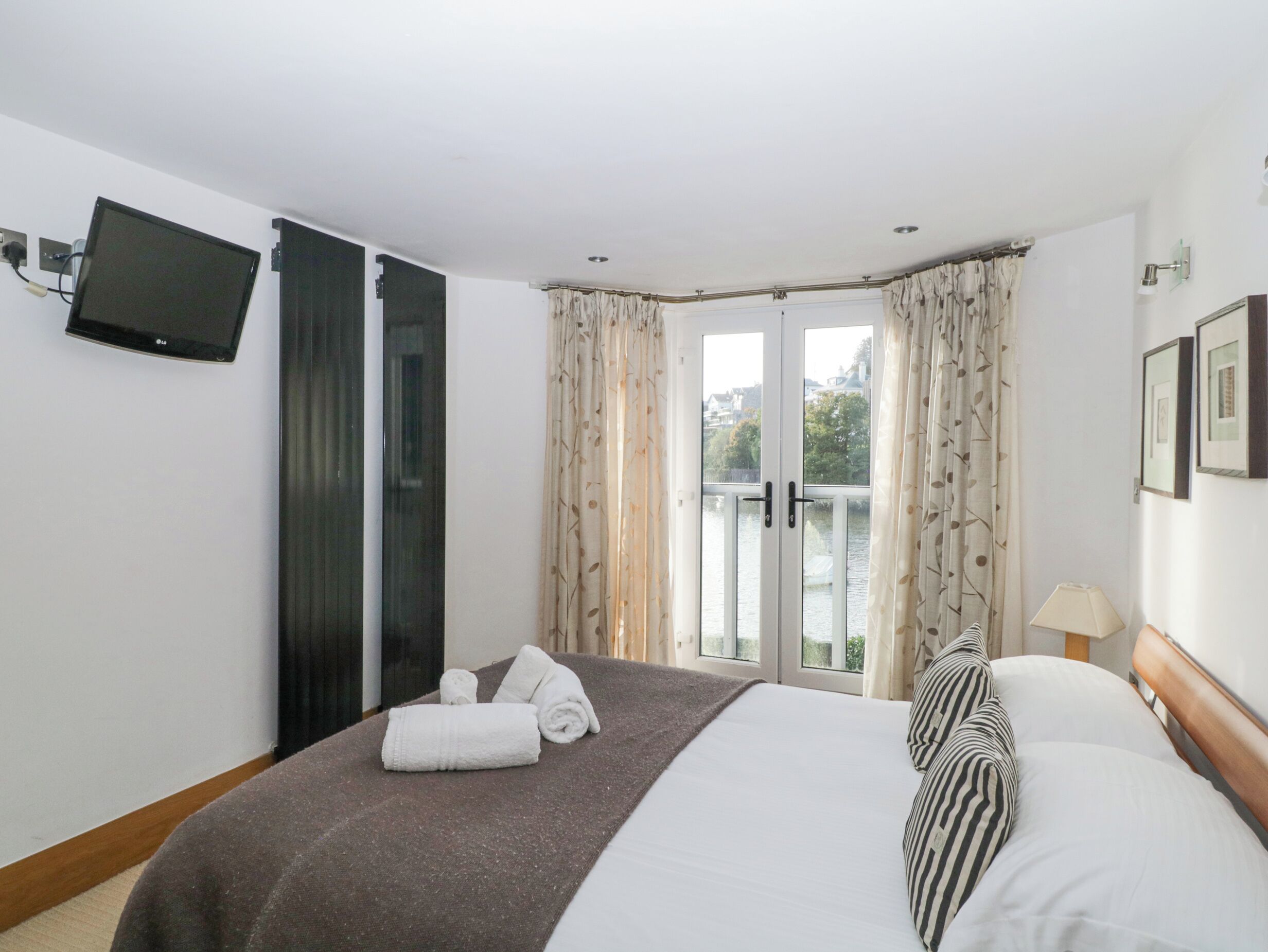 Ein Hotelzimmer mit Bett, einem an der Wand montierten Fernseher, einem Fenster mit Vorhängen und Blick ins Freie.