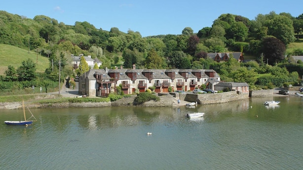 A row of traditional stone houses by a calm lake, with boats docked nearby.