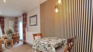 A dining area with a table set for two, flanked by wooden chairs, a wooden side table, and a potted plant. - Little Willesleigh (Barnstaple)
