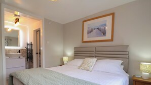 A bedroom with a bed, bedside lamps, a nightstand, a framed picture on the wall, and a bathroom with a sink and towel rack. - Little Willesleigh (Barnstaple)