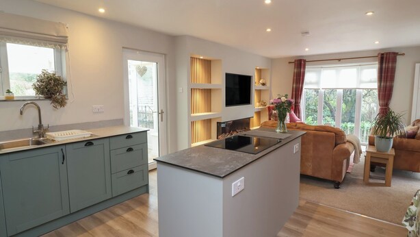 A modern kitchen with a central island, a dining area with a sofa, and a TV mounted on the wall. - Little Willesleigh (Barnstaple)