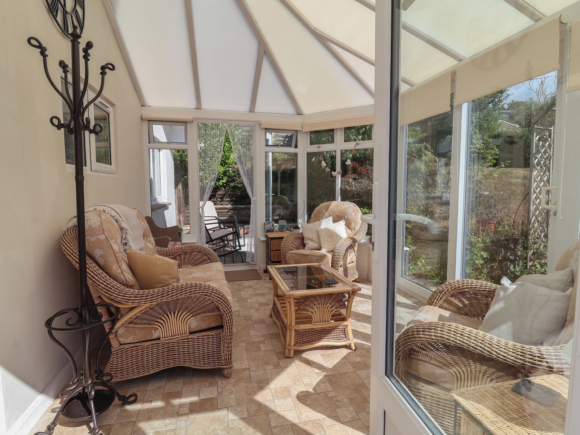 A sunlit room with wicker furniture, a glass table, and a view of greenery outside.