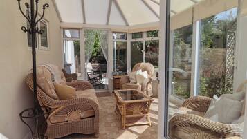 A sunlit room with wicker furniture, a glass table, and a view of greenery outside.