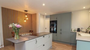 A modern kitchen with a central island, light grey cabinets, and a wooden accent wall. - Little Willesleigh (Barnstaple)