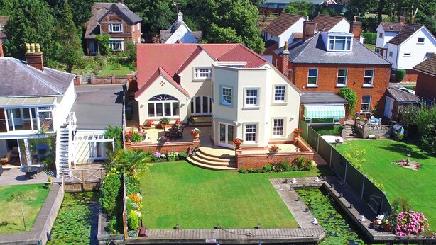 A large house with a red roof, a front porch, and a small pond with lily pads. - The Little House (Norwich)