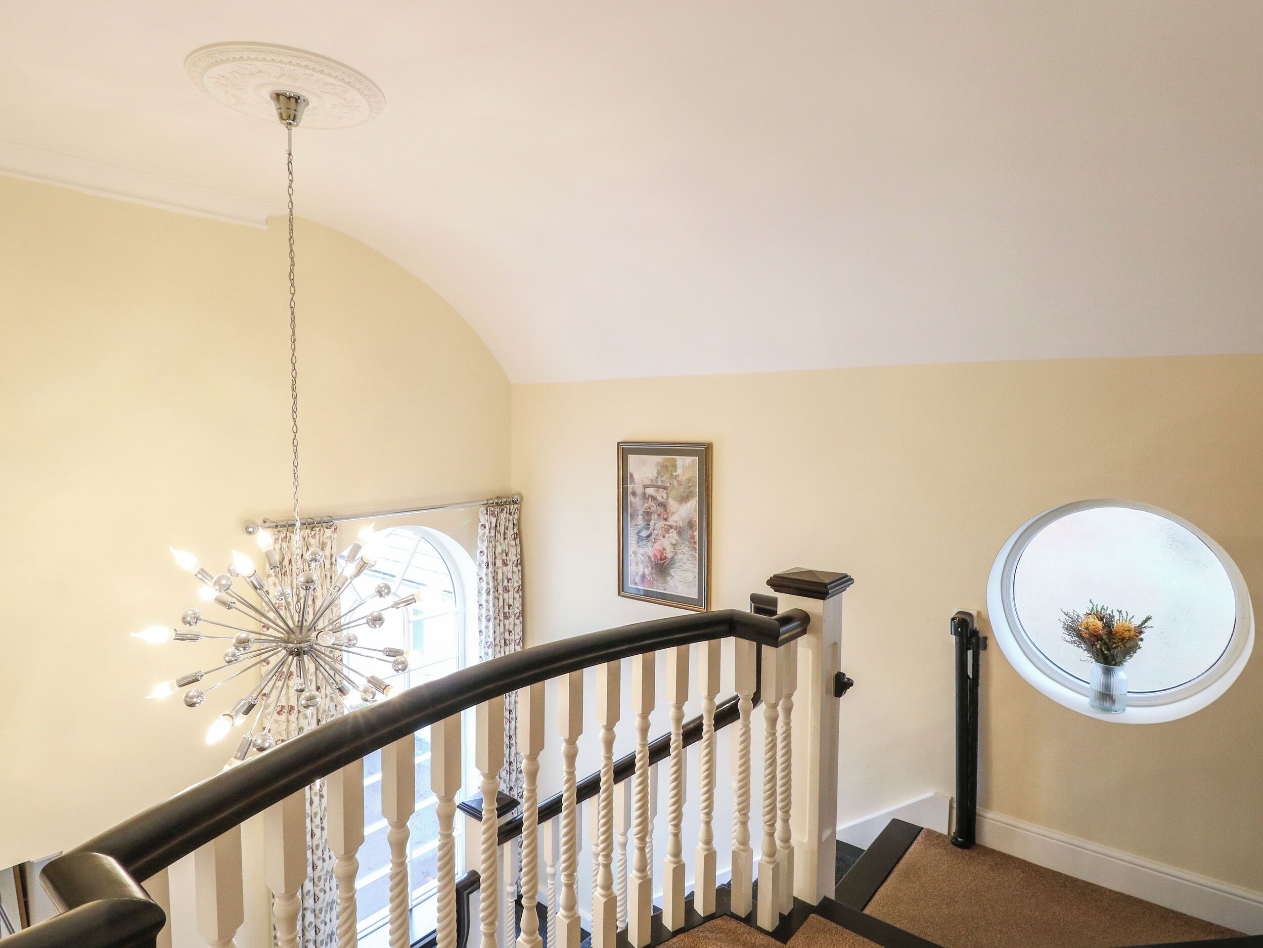 Eine Treppe mit einem Chandelier, einem gerahmten Bild und einem Fenster mit einem Blumenstrauß.