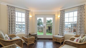A room with wicker furniture, a glass table, and a view of a garden through a door. - The Little House (Norwich)