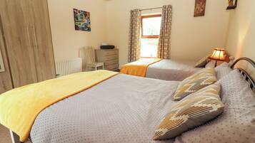 A bedroom with two beds, a dresser, a chair, a window with curtains, and a wall with a decorative alphabet piece.