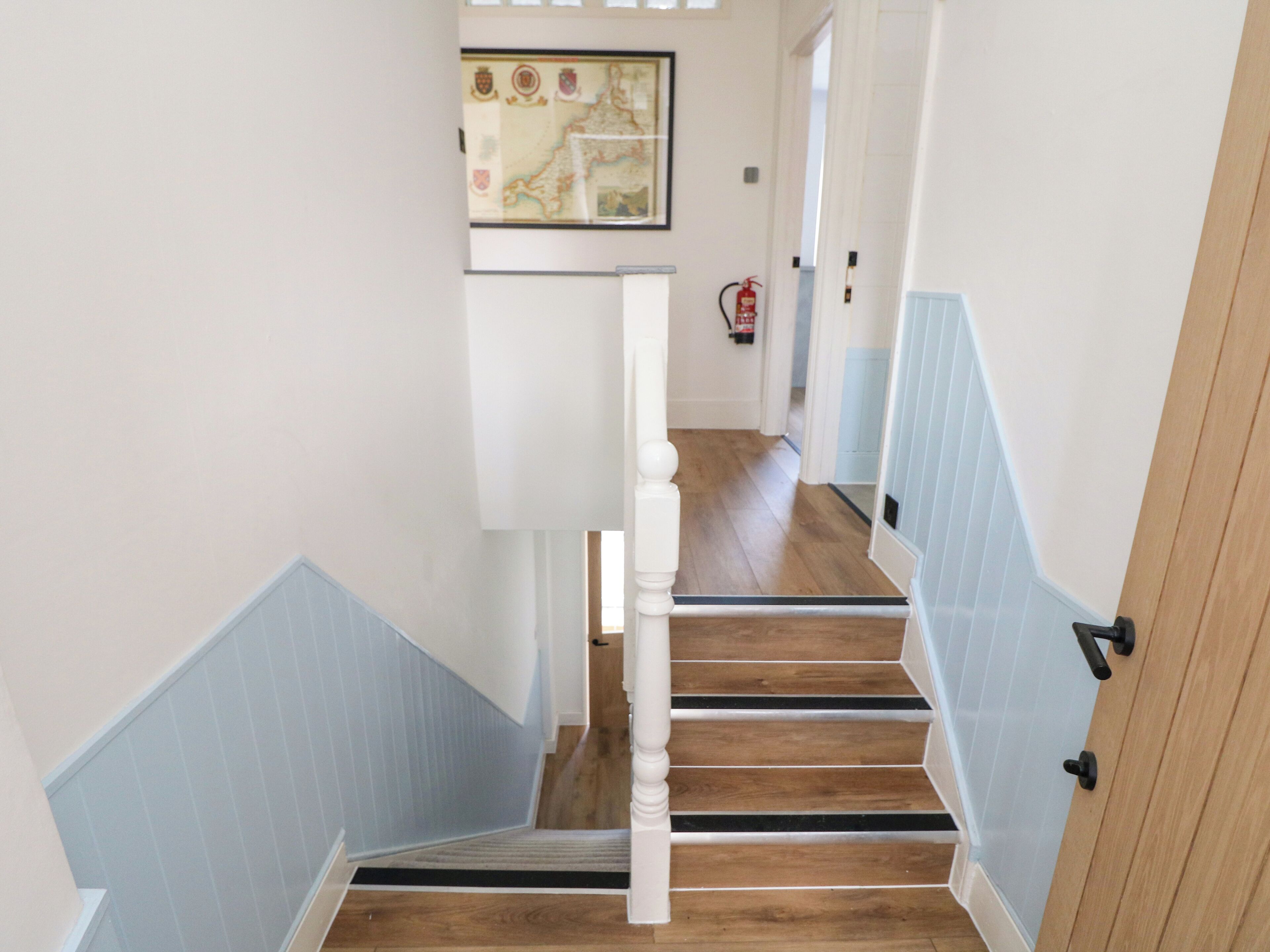A staircase with wooden steps and white balusters, leading to a landing with a framed map.