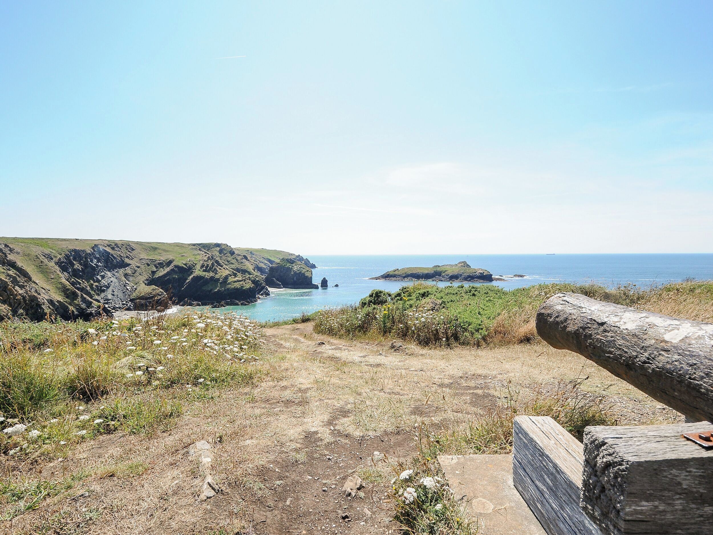 Un paysage côtier caractérisé par un ciel dégagé, des falaises rocheuses et une vue lointaine sur la mer.