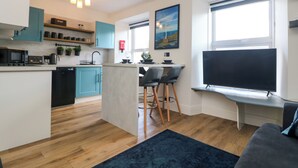 Una cocina moderna con una isla central, un comedor con sillas, un televisor de pantalla plana y un ventanal grande.