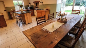Een ruime keuken met een houten eettafel, barstoelen en uitzicht op de tuin door grote ramen.