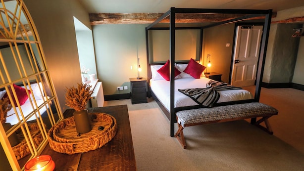 Een hemelbed met een bankje, een nachtkastje, een spiegel en een kaars op een houten dressoir.