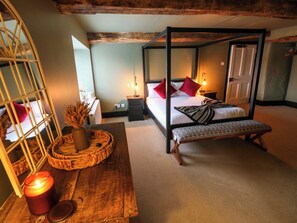 A four-poster bed with a bench, a bedside table, a mirror, and a candle on a wooden dresser.