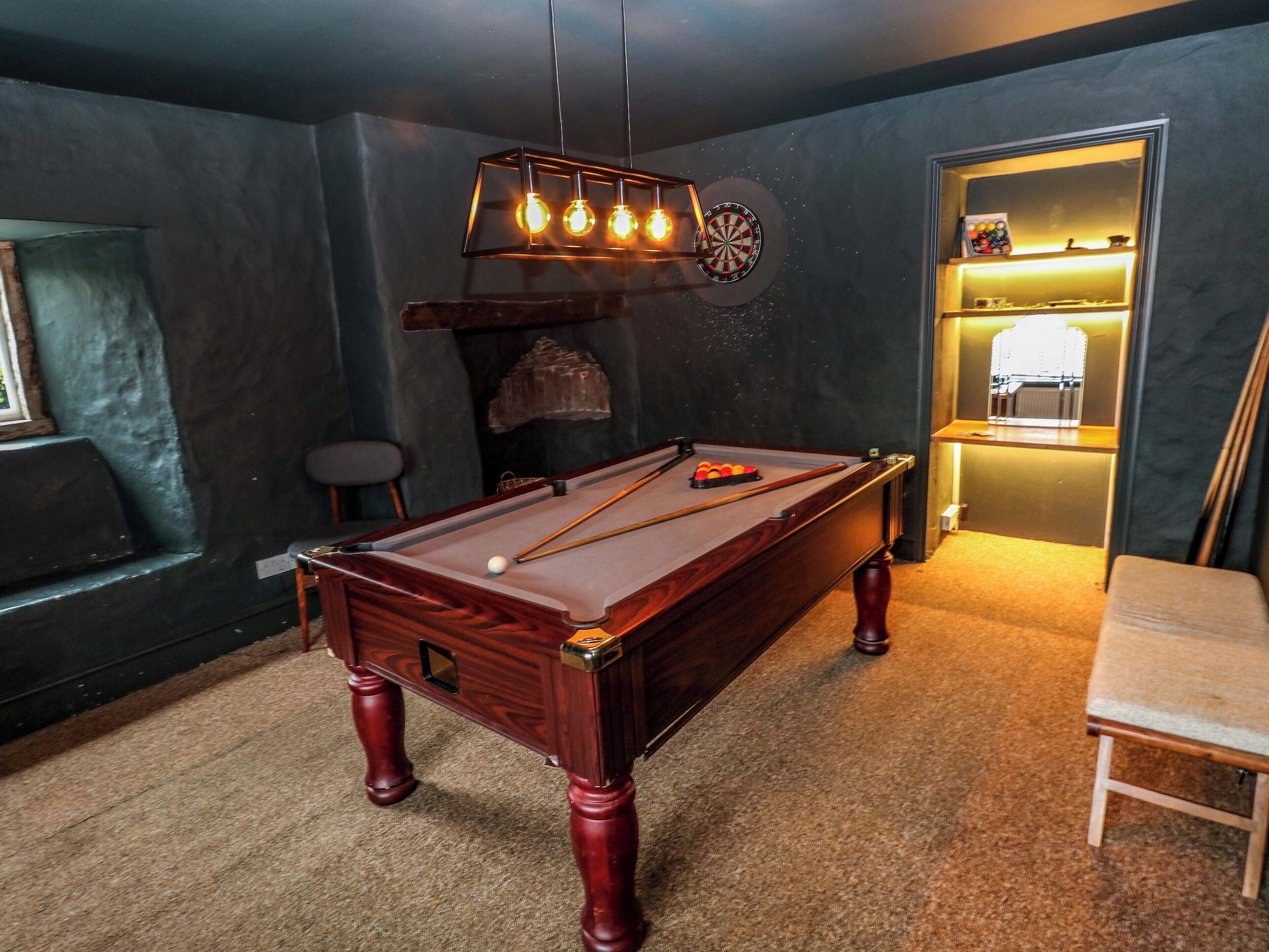 A pool table with a dartboard and a billiards rack in a room with dark walls and a carpeted floor.