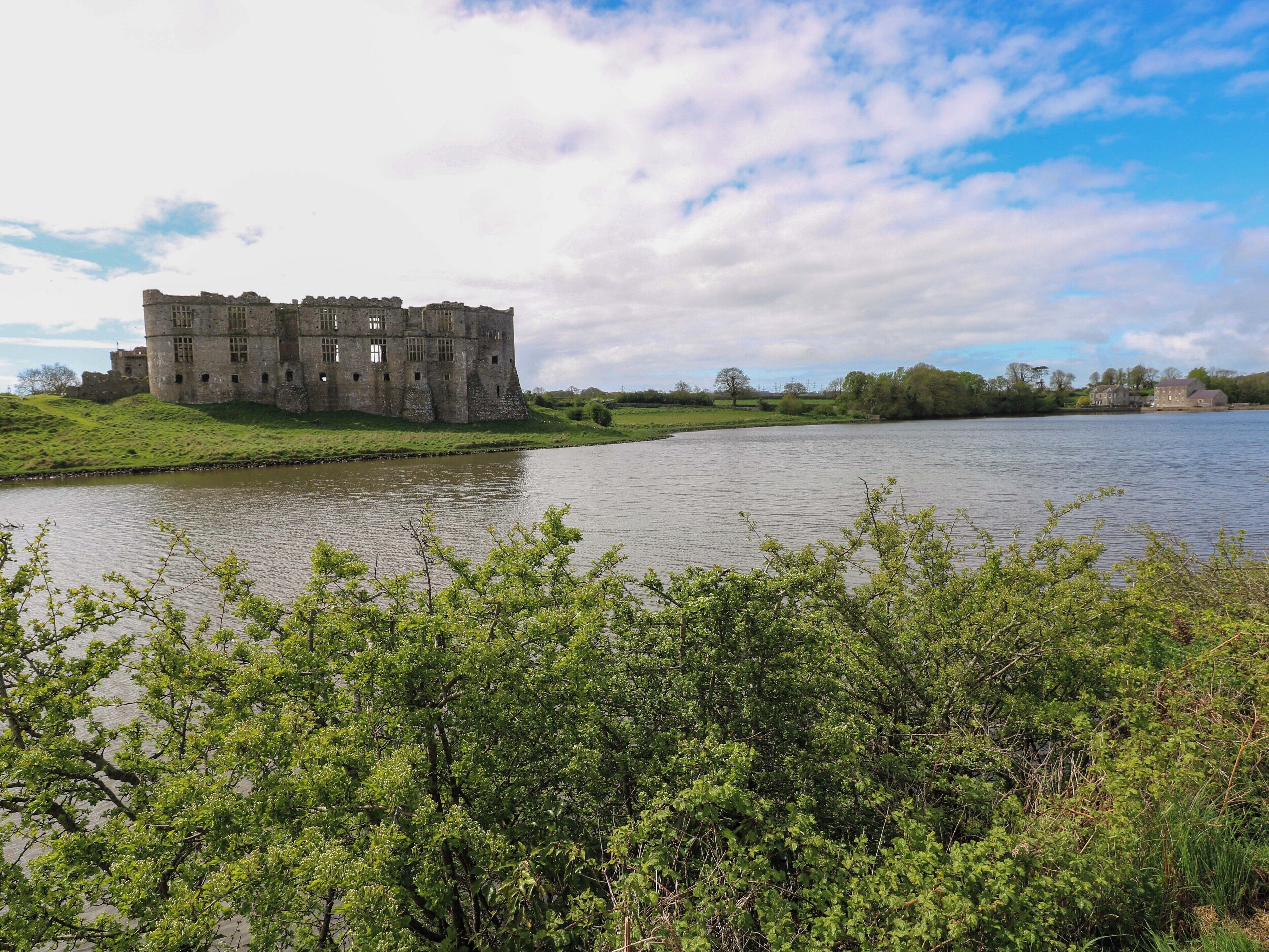 Un castillo histórico junto a un lago, con un primer plano de césped y cielo despejado.
