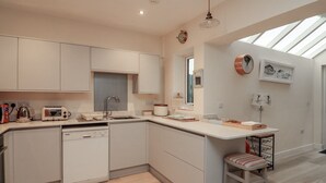 A modern kitchen with a dishwasher, a toaster, and a sink. There is a window above the sink and a clock on the wall. - Full Deck (Dartmouth)