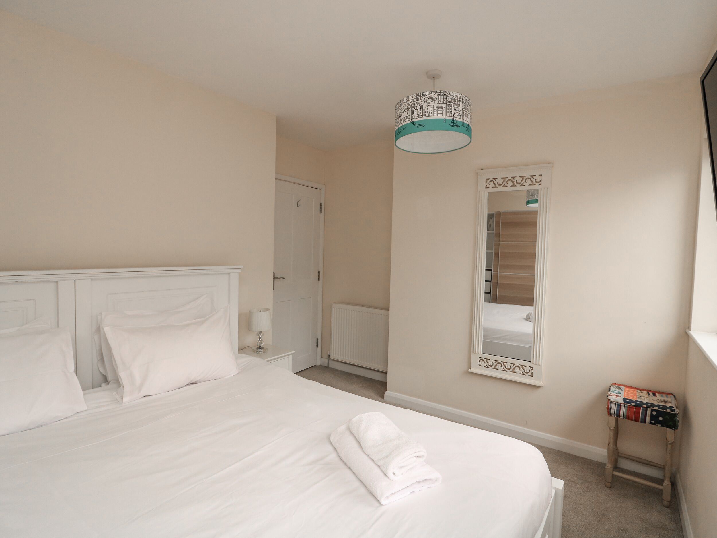 A neatly made bed with white linens, a white headboard, and a folded towel on the bed.