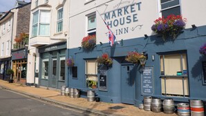 A building with a sign reading "Market House Inn" and features large flower baskets, a flag, and several barrels on the sidewalk. - Full Deck (Dartmouth)