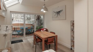 A dining area with a wooden table and chairs, a pendant light, and a large window with a view of an outdoor seating area. - Full Deck (Dartmouth)