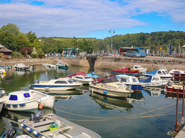Un puerto deportivo con varias embarcaciones amarradas, un puente al fondo y un autobús pasando.