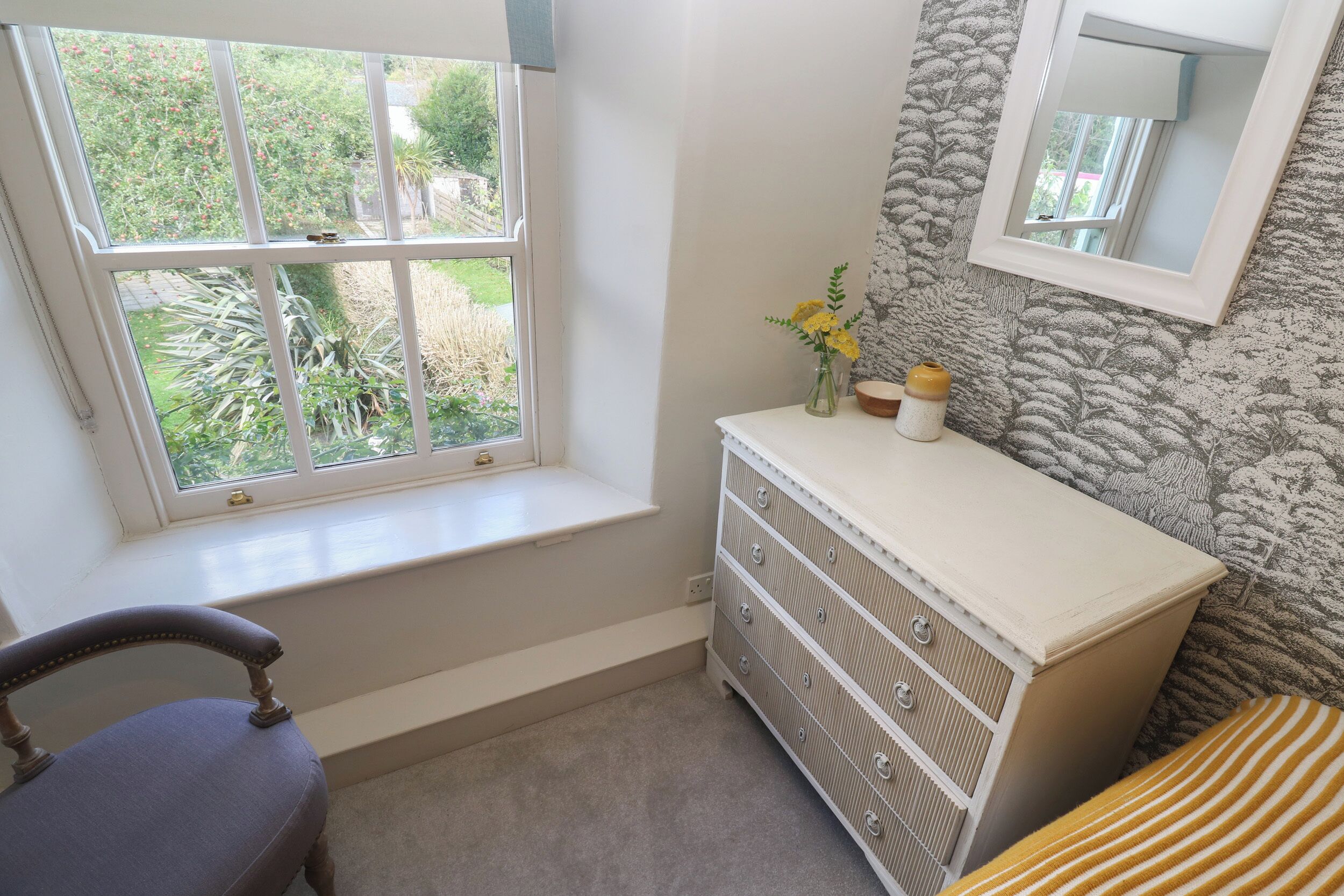 A bedroom with a window, a dresser, a chair, and a bed.