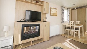 Ett modernt vardagsrum med en platt-TV, en öppen spis, träskåp, en matplats med stolar och en spegel på väggen.
