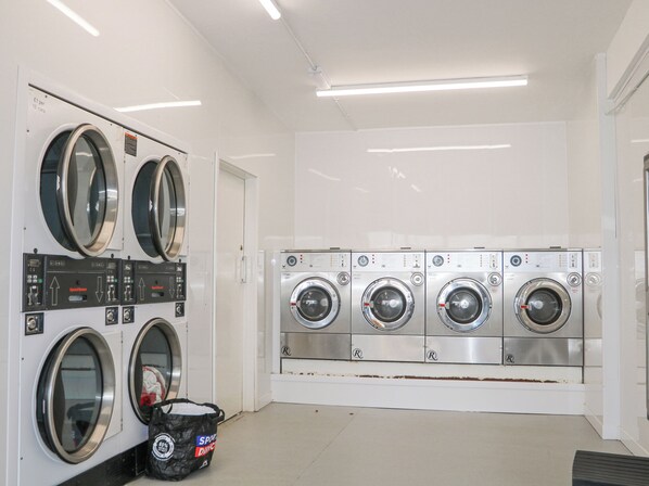 A laundry facility with multiple washing machines and dryers, a door, and a bag of detergent on the floor. - 610 Caravan (Bognor Regis)