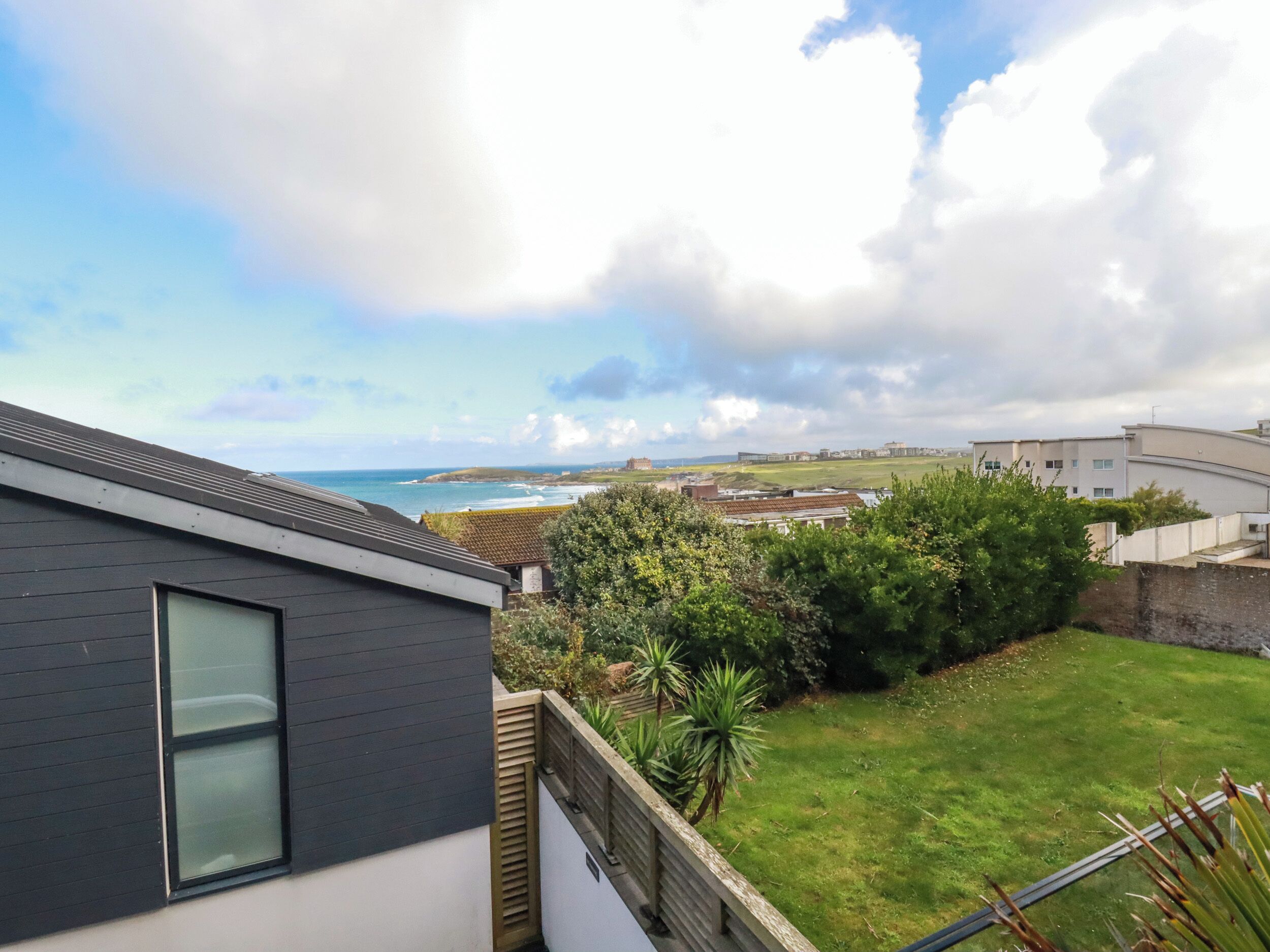 A residential area with a view of the sea, a grassy lawn, and a modern building with a dark facade and large windows.