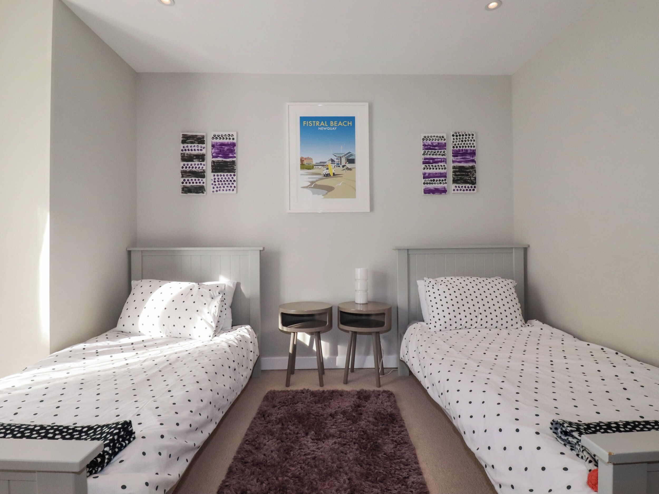 A bedroom with two beds, a small table, a rug, and a poster on the wall.