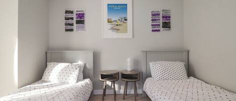 A bedroom with two beds, a small table, a rug, and a poster on the wall.