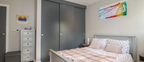 Ein Schlafzimmer mit Bett, Kommode, Kleiderschrank, Nachttisch und einem Bild an der Wand.