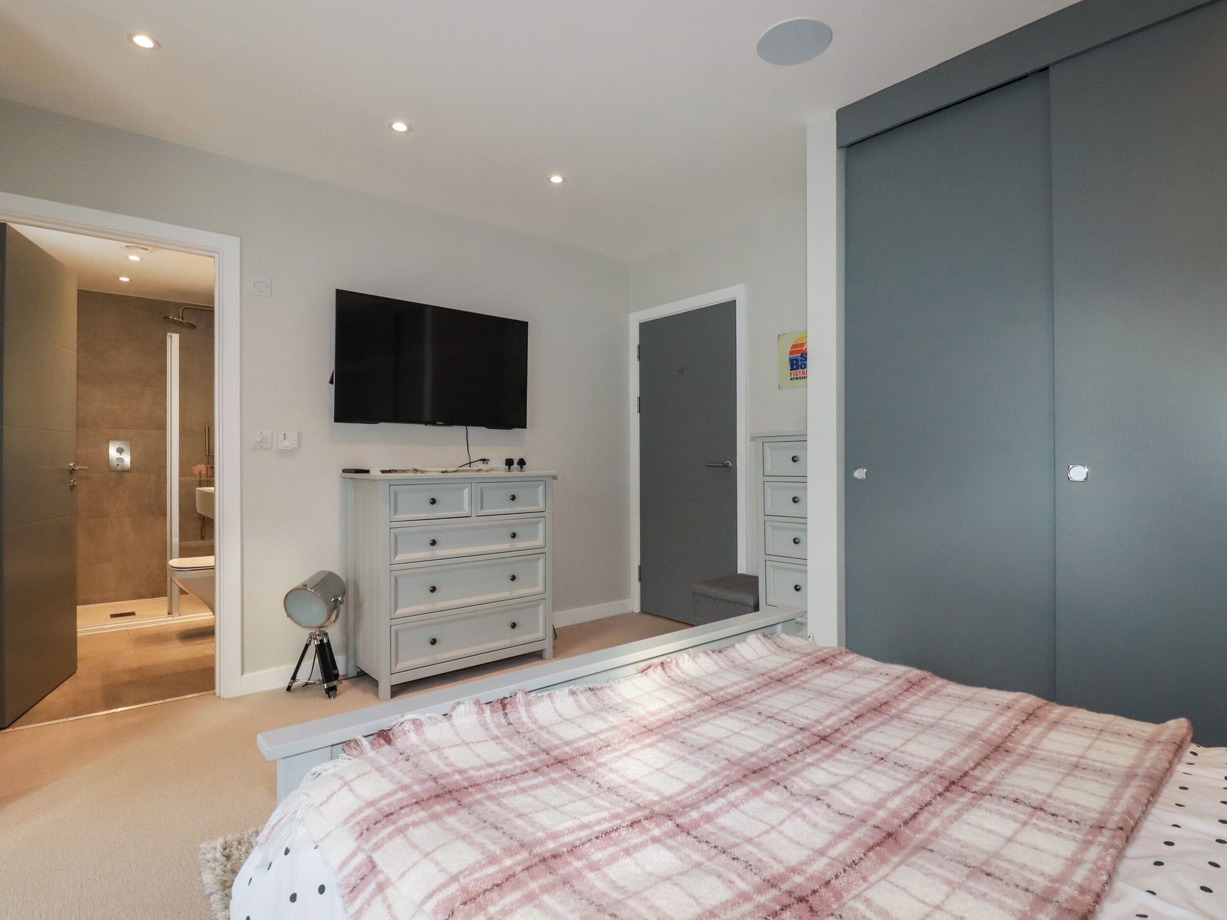 A bedroom with a bed, a dresser, a television, a mirror, and a door leading to a bathroom.